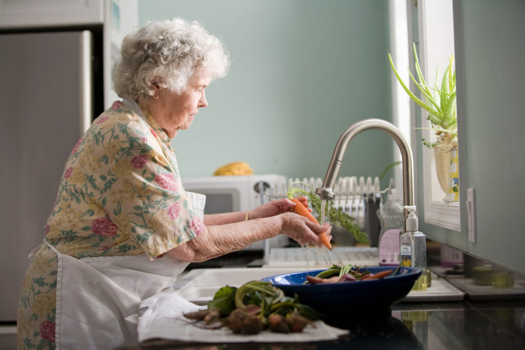 Une femme âgée prépare de la nourriture dans la cuisine.